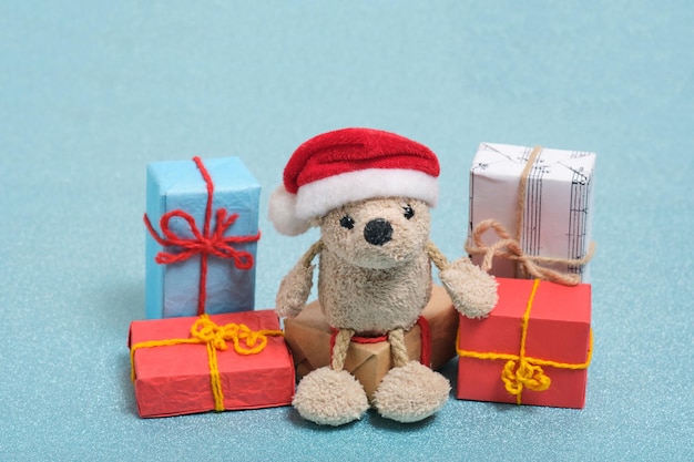 Kleine teddybeer in een kerstman hoed zit op dozen met kerstcadeaus. Op een blauwe achtergrond.