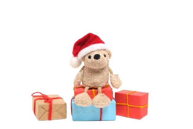 Kleine teddybeer in een kerstman hoed zit op dozen met kerstcadeaus. Op een witte achtergrond.