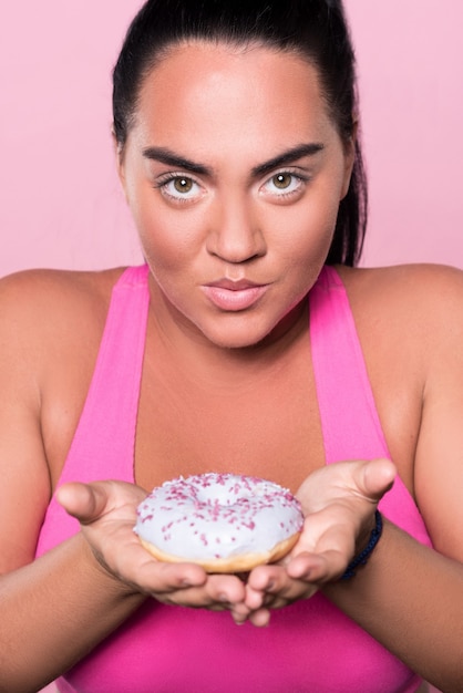 Kleine verleiding. Sluit omhoog van mooie mulatdame die leuke smakelijke doughnut houdt en vooruit kijkt.