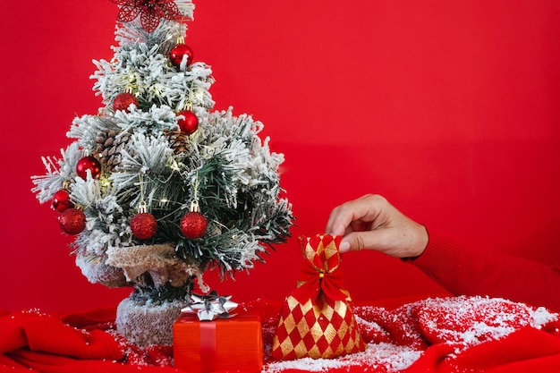 Kleine versierde kerstboom en vrouwelijke hand die een cadeautje aanbiedt kopieer ruimte op rode achtergrond