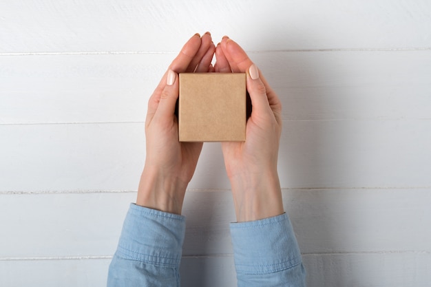 Kleine vierkante kartonnen doos in vrouwelijke handen. Bovenaanzicht, wit oppervlak