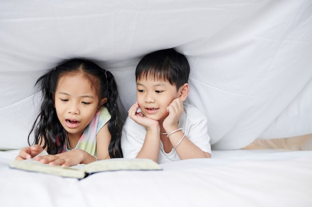 Kleine Vietnamese broer en zus liggen onder de deken en lezen een boek