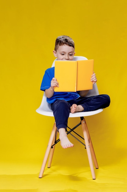 Kleine vrolijke blonde jongen met groene ogen 56 jaar oud in een stijlvol blauw T-shirt met boek en lezend op gele muur achtergrond kinderstudio portret