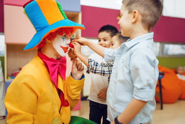 Kleine vrolijke jongen raakt de neus van de rode clown aan, kinderen spelen samen.