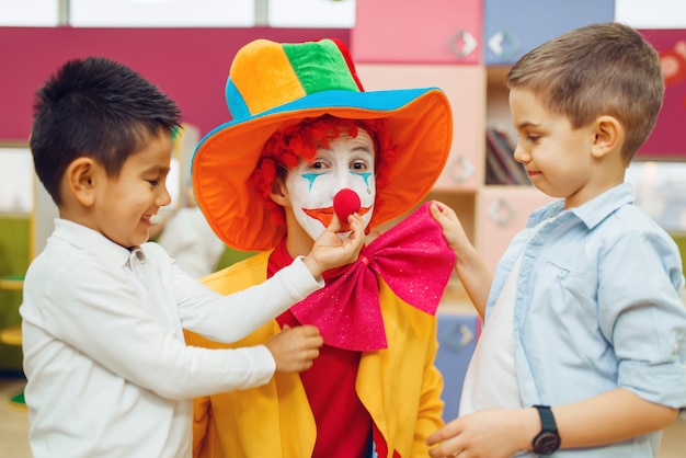 Kleine vrolijke jongen raakt de neus van de rode clown