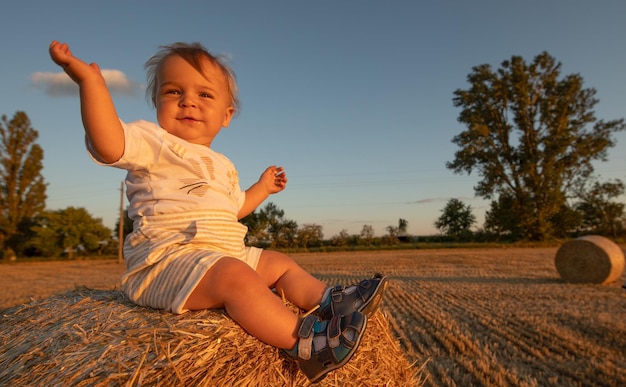 Kleine vrolijke jongen zittend op een grote ronde baal stro tegen de achtergrond van de blauwe lucht