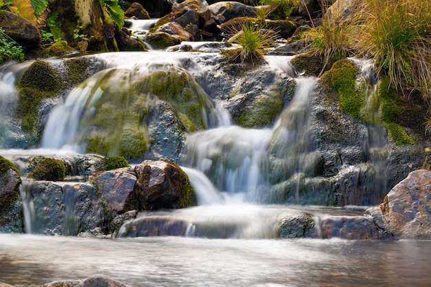 Kleine waterval in park met prachtig glad water. Kleine waterval in bergbos met zijdeachtig schuimend water.