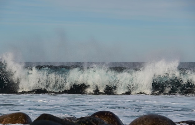 Kleine zeegolven breken tegen de stenen van de kust een heldere zonnige dag en wit schuim van de golven smeltende gletsjers als een milieu-impact van luchtvervuiling