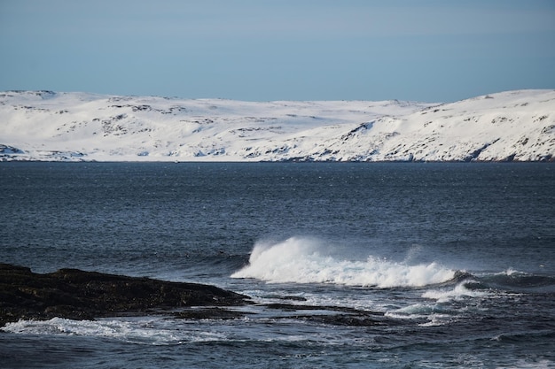 Kleine zeegolven breken tegen de stenen van de kust een heldere zonnige dag en wit schuim van de golven smeltende gletsjers als een milieu-impact van luchtvervuiling
