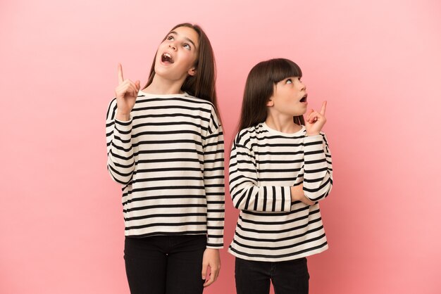 Kleine zusters meisjes geïsoleerd op roze achtergrond denken een idee met de vinger omhoog