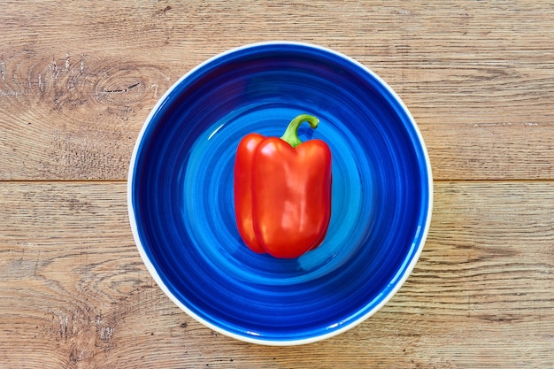 Kleur stilleven - rode paprika op een diepblauwe plaat op een houten tafelblad