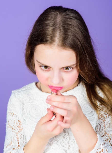 Kleuren leren met lippenstift Schattig klein kind dat naar lippenstift kijkt Schattig klein meisje dat lippenstiftbuis vasthoudt Schoonheidsmodel dat roze lippenstift voor haar lippen kiest