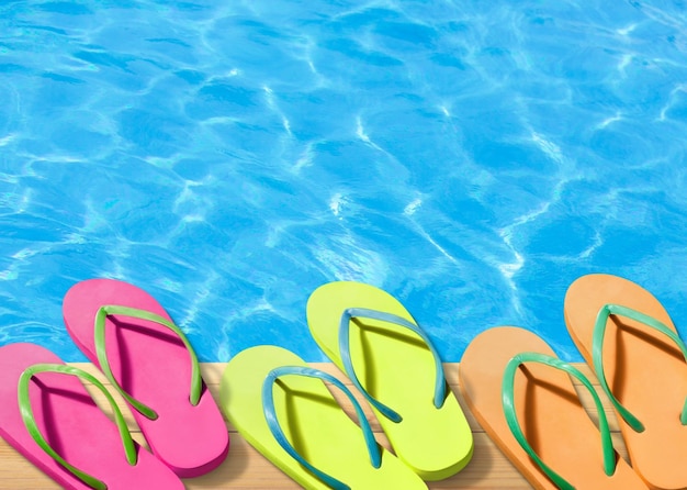 Foto kleurige flip-flops zitten aan de rand van een zwembad.