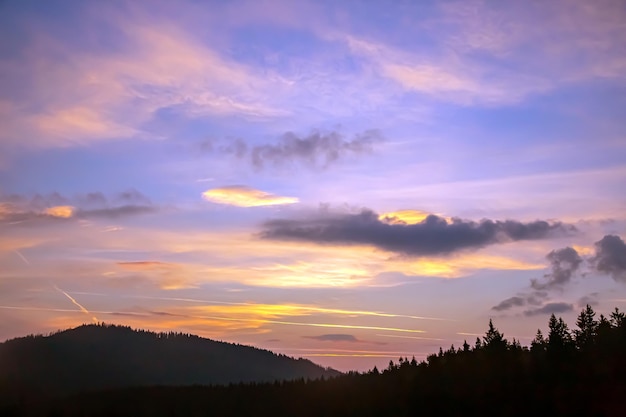 Kleurige wolken aan de hemel bij zonsondergang tegen de achtergrond van een bergachtig bosgebied
