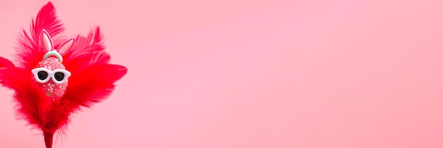 Foto kleurrijk ei met konijnenoren in zonnebril in rode veren op een roze achtergrond happy easter promotie sjabloon voor spandoekmodel close-up banner