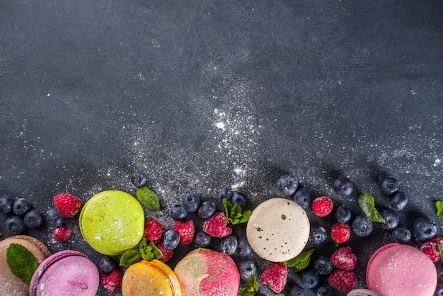 Kleurrijk Frans macarondessert. Set van verschillende smaken en kleuren macaron-koekjes met bessen, suikerpoeder en munt op donkergrijze stenen achtergrond