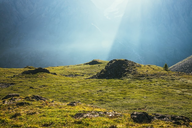 Kleurrijk groen landschap met rotsen en heuvels op de achtergrond van een gigantische bergmuur in zonlicht. Minimalistisch levendig zonnig landschap met zonnestralen en zonnevlam. Minimaal uitzicht op de Alpen. Schilderachtig minimalisme.