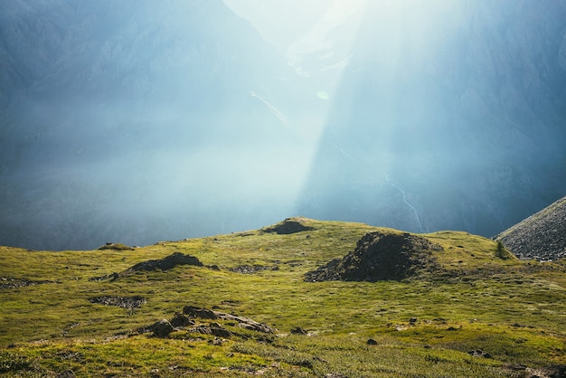 Kleurrijk groen landschap met rotsen en heuvels op de achtergrond van een gigantische bergmuur in zonlicht. Minimalistisch levendig zonnig landschap met zonnestralen en zonnevlam. Minimaal uitzicht op de Alpen. Schilderachtig minimalisme.