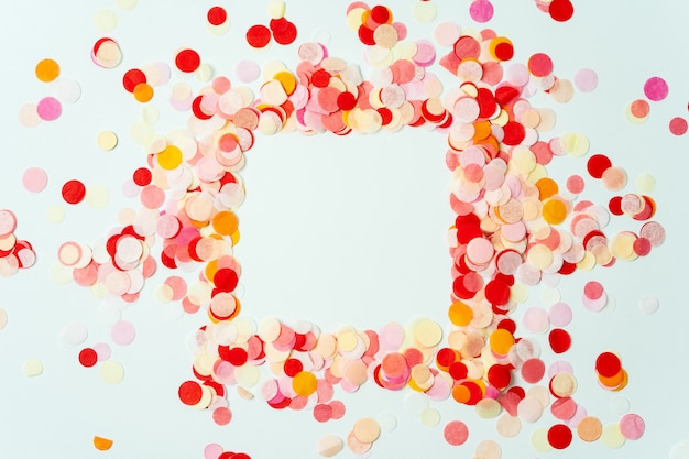 Kleurrijk kader dat met rode en oranje feestelijke confettien op pastelkleurachtergrond wordt gemaakt