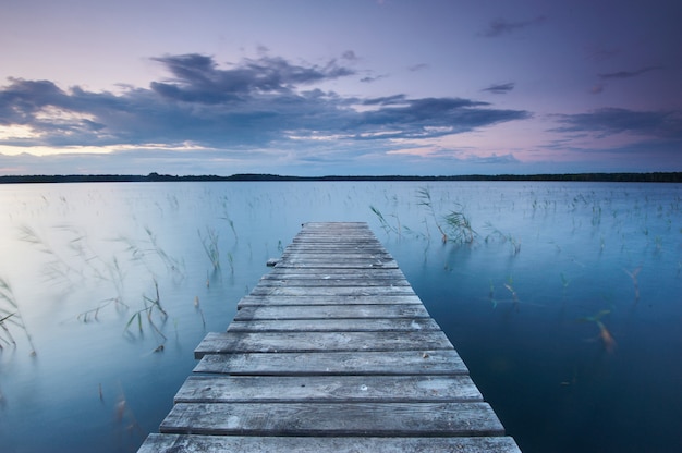 Kleurrijk landschap met lucht en houten steiger weerspiegeld in het meer bij avond