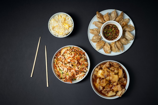 Kleurrijk palet van Aziatische afhaalmaaltijden - garnalensalade, zoete knapperige kip, rijst en gebakken dumplings op zwarte achtergrond