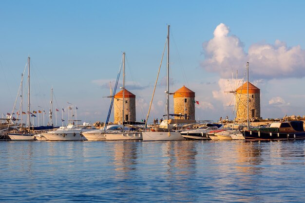 Kleurrijk panoramisch uitzicht op windmolens met jachten in de haven van Mandraki bij zonsondergang Rhodos, Griekenland