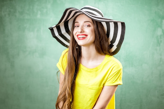 Kleurrijk portret van een mooie vrouw in geel t-shirt en gestreepte hoed op de groene achtergrond