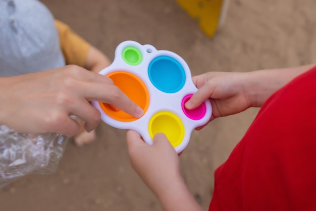 Kleurrijk trendy antistress zintuiglijk speelgoed fidget push pop it en eenvoudig kuiltje in kinderhanden kinderen delen speelgoed en spelen samen