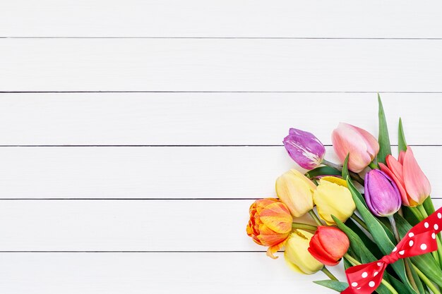 Kleurrijk tulpenboeket dat met lint op witte houten achtergrond wordt verfraaid