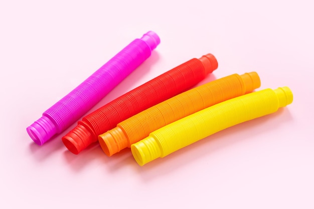 Kleurrijke anti-stress fidget push pop buis zintuiglijk speelgoed voor kinderen op roze achtergrond. bovenaanzicht, plat gelegd. close-up van creatief spel met populaire plastic flexibele heldere golfpijp.