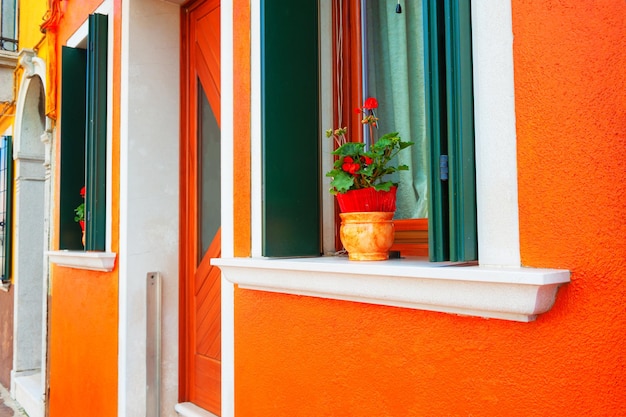 Kleurrijke architectuur in Burano-eiland, Venetië, Italië. Oranje geschilderde gevel van het huis en ramen met bloemen.