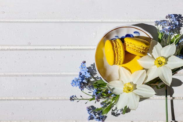 Kleurrijke bitterkoekjes en bloemen op witte houten tafel zoete macarons bovenaanzicht met kopie ruimte voor uw tekstlekker dessert plat lag en narcissen en vergeet-me-niet bloemen