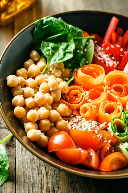 Kleurrijke buddha bowl met kikkererwten, wortelen, tomaten, komkommers, radijs en paprika op houten tafel. vegetarische salade.