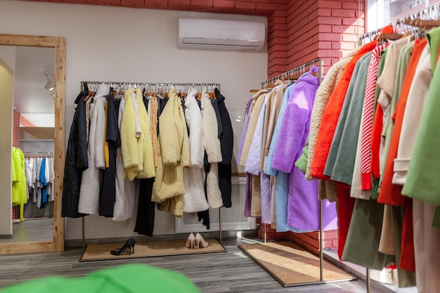 Kleurrijke damesjurken, jassen, broeken en andere kleding op hangers in een winkel.