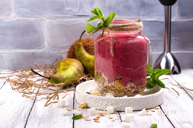 Kleurrijke detox-zomersmoothie met rode bessen, peren, muesli en droge kokosblokjes