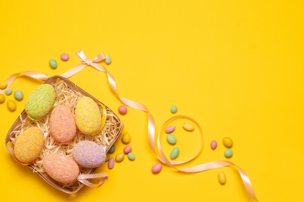 Kleurrijke eieren in een rieten mand met gekleurde decoratie op een gele achtergrond