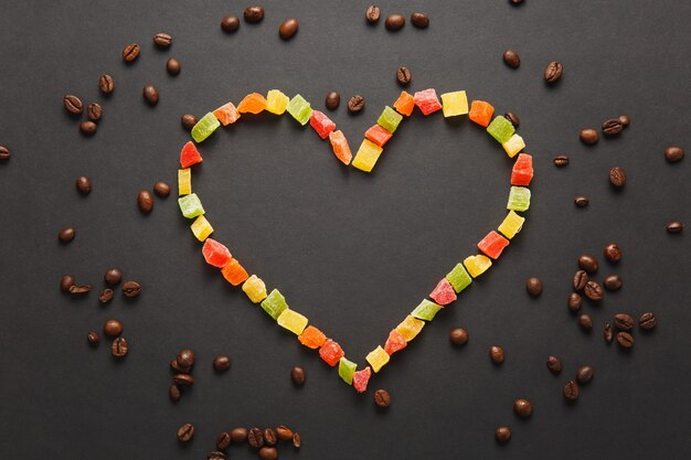 Kleurrijke gekonfijte vruchten in de vorm van een hart met bruine koffiebonen geïsoleerd op een zwarte achtergrond voor design. Saint Valentine's Day-kaart op 14 februari, vakantieconcept. Kopieer ruimte voor advertentie.