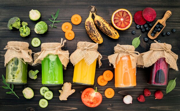 Foto kleurrijke gezonde smoothies en sappen in flessen met vers tropisch fruit en supervoedsel op houten achtergrond