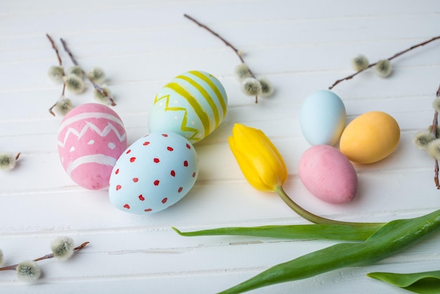 Kleurrijke heldere paaseieren met gele tulp met de hand geschilderd op een witte houten achtergrond Feestelijke lentekaart