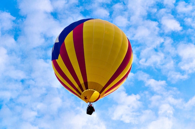 Kleurrijke heteluchtballon die over blauwe hemel met witte wolken vliegt.