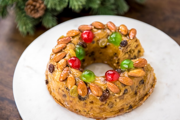 Kleurrijke kerst fruitcake gegarneerd met amandelen en glace kersen op witte schotel