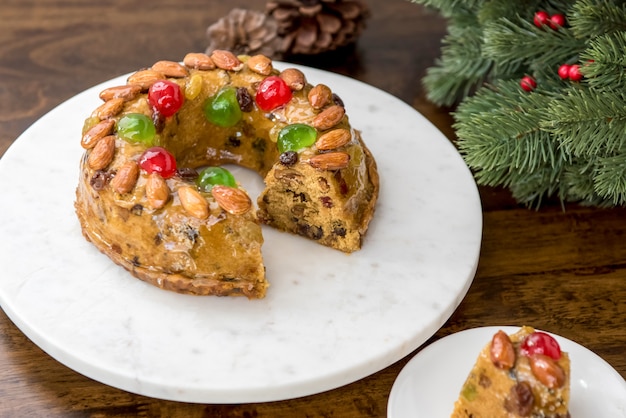 Kleurrijke kerst fruitcake gegarneerd met amandelen en glace kersen op witte schotel