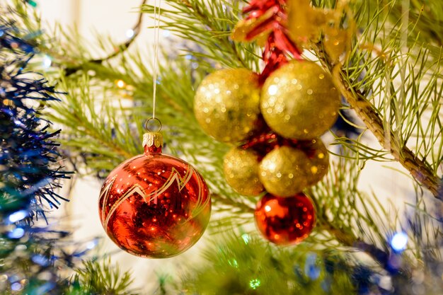 Kleurrijke kerstballonnen op een kerstboom tegen de achtergrond van glanzende slingers. Kleurrijke ballen omgeven door takken van de kerstboom. Kerstconcept.