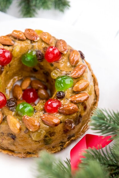 Kleurrijke Kerstmisvruchtencake met groene pijnboom en rode lintdecoratie