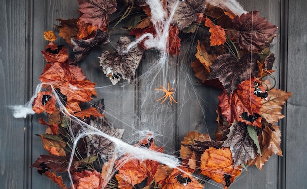 Kleurrijke krans voor halloween opknoping op houten huisdeur gemaakt van oude oranje esdoornbladerenspinnenwebverfraaien van verandahome buitentstraatdecoratieentertainment voor kinderenhorror sfeer