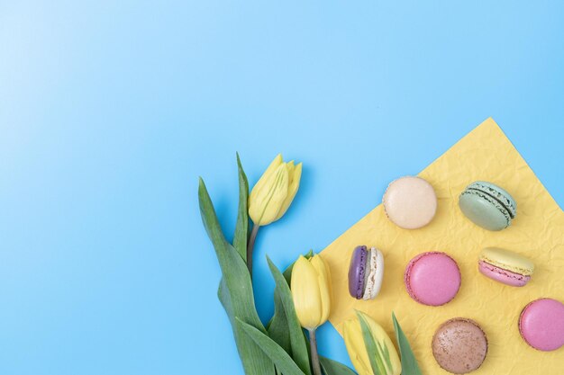 Kleurrijke macarons en tulpen met geel papier op een blauwe achtergrond