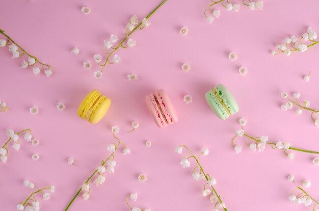 Kleurrijke macarons of bitterkoekjes versierd met bloeiende lelietje-van-dalenbloemen op pastelroze. Zoet Frans dessertconcept. Plat leggen