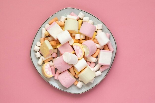 Kleurrijke marshmallows op een witte vierkante plaat geïsoleerd op een roze achtergrond. Close-up van de textuur van een pluizige marshmallow.