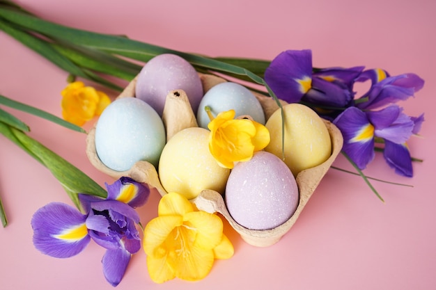 Kleurrijke paaseieren in een bakje en bloemen op een roze achtergrond. Bovenaanzicht