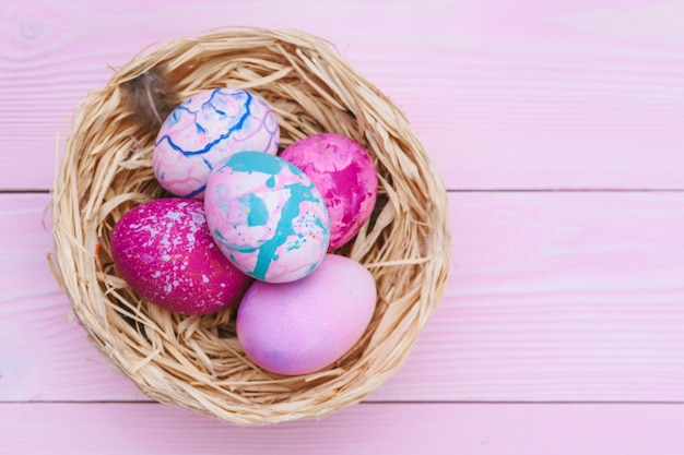 Kleurrijke paaseieren in een nest op roze houten tafel